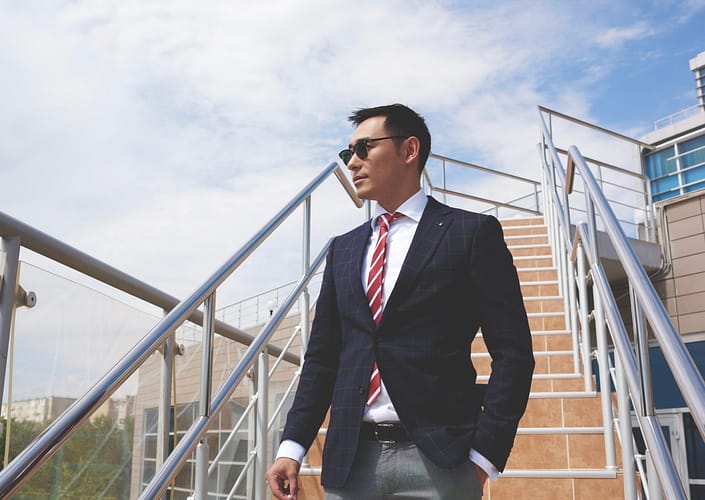 Portrait of a successful smart asian men dressed in elegant clothes standing on the street while having cigarette during work break, young confident businessman in formal wear resting after hard day